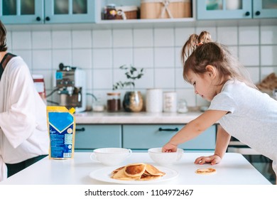 Little cute girl on kitchen is taking pancake from table. - Shutterstock ID 1104972467
