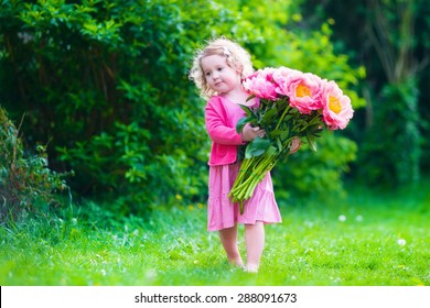 Little cute girl with peony flowers. Child wearing a pink dress playing in a summer garden. Kids gardening. Children play outdoors. Toddler kid with flower bouquet for birthday or mother's day.