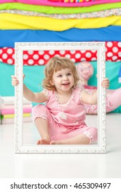 Little cute girl in a pink suit sitting on the floor and smiling over a wooden white frame.