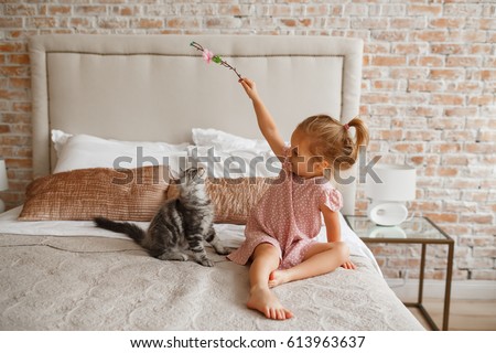 Little cute girl playing with kitten on sofa at home. Lifestyle child photo