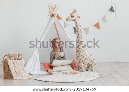 Little cute girl plays with soft toys near the wigwam in the bright children's room. Funny cute little girl having fun in the children's room.