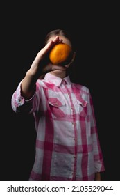 Little Cute Girl Posing With Tangerine In The Studio. Photo Isolated On Black Background With One Light Source. The Child Covers His Face With Tangerine.