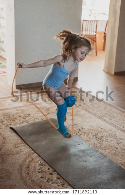 Little cute girl\
is practicing gymnastics at home. Online training. Jumping rope.\
Quarantine. Stay at\
home.