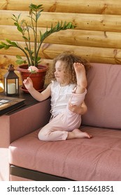 Little Cute Girl And Rose Flower. She With Curly Hair, In Pajamas And Barefoot Sitting On Couch. Happy Childhood.