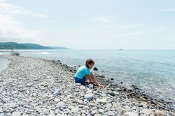 Little Cute Girl Sits On A Pebble Beach And Plays With Pebbles