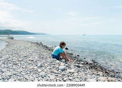 Little cute girl sits on a pebble beach and plays with pebbles - Powered by Shutterstock