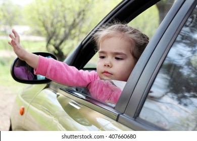 Little Cute Girl Sitting Behind The Wheel Of A Car And Waving Her Hand Saying Goodbye, Outdoors, Family Travel Concept