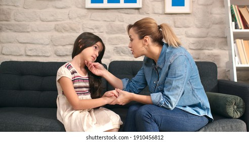 Little Cute Girl Talking To Her Mother Sitting On Sofa At Home. Loving Happy Mother, Sad Cute Kid Comforting Her Daughter, Making Her Laugh. Lifestyle At Home.