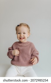 Little Cute Happy Baby Girl In A Pink Sweater And White Pants On A White Background. Smiling Child.