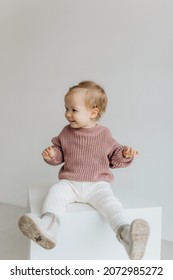 Little Cute Happy Baby Girl In A Pink Sweater And White Pants On A White Background. Smiling Child.