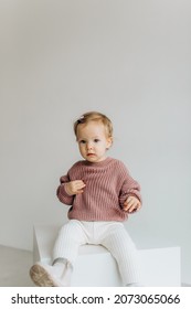 Little Cute Happy Baby Girl In A Pink Sweater And White Pants On A White Background. Smiling Child.