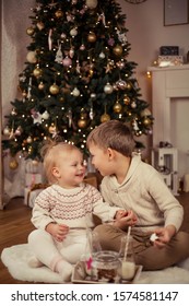 Little cute happy boy and girl sit near the Christmas tree and drink milk with Christmas cookies. Christmas. New Year. Cozy.