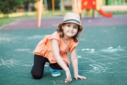 Little Cute Happy Girl Draws Painting A Chalk On Pavement Asphalt On Ground On Playground. Creative Children Summer Activity.