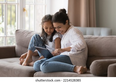 Little cute Indian girl and mom use digital tablet, resting together at home, buying goods through retail services webstore, learn new amusing application seated on cozy sofa, enjoy modern tech usage - Powered by Shutterstock