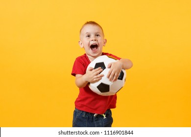 Little Cute Kid Baby Boy 3-4 Years Old, Football Fan In Red T-shirt Holding In Hand Soccer Ball Isolated On Yellow Background. Kids Sport Family Leisure Lifestyle Concept. Copy Space Advertisement