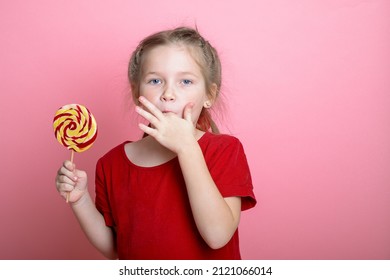 Little Cute Kid Girl Lick Fingers. Child With Lollipop Sugar Candy. Sticky Dirty Fingers And Girl Licks Them Isolated On Pink Background. Tasty Food.