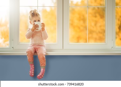 Little Cute Kid Girl Sitting By Window Holding Cup Of Hot Drink Cocoa Enjoying Autumn Forest Background. Season Beauty Fashion Children Concepts. Fall Season