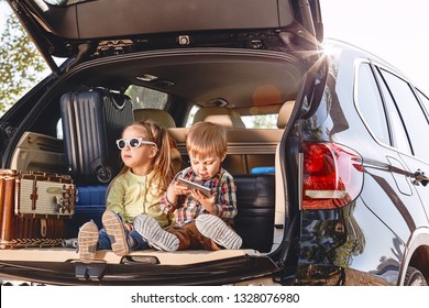 Little Cute Kids Having Fun In The Trunk Of A Black Car With Suitcases. Family Road Trip