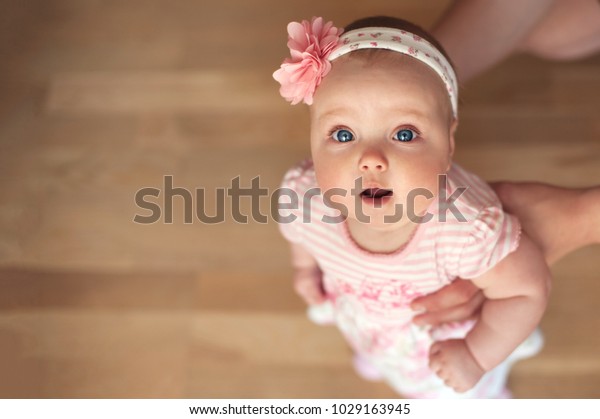 青い目をした小さくてかわいい金髪の女の子 赤ちゃん ピンクのドレスと花を頭に着け 歩き始め 父親が手伝う の写真素材 今すぐ編集