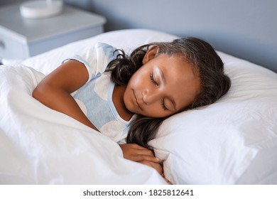 Little Cute Mixed Race Girl Lying On Bed. Portrait Of Little Indian Child Sleeping Under White Blanket. Close Up Face Of Adorable Female Kid Sleeping Deeply And Dreaming With Closed Eyes In Bedroom.