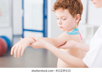 Little Cute Red Head Boy Having Arm Problem After Injury. Physical Therapist Treating The Patient With Exercises