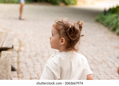 Little cute red-haired girl looks away in surprise while standing on a cobbled road