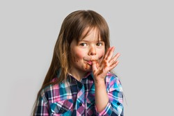 Little Cute Sly Girl Got Her Chocolate Fingers Dirty And Licks Them Isolated On A Light Gray Background.