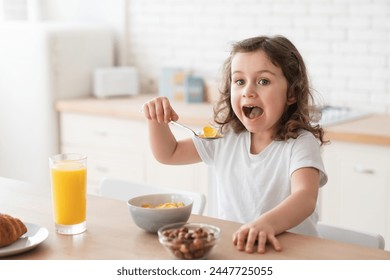 Little cute small daughter girl learning how to eat with a spoon, eating corn flakes in the kitchen, having breakfast, healthy eating habits - Powered by Shutterstock