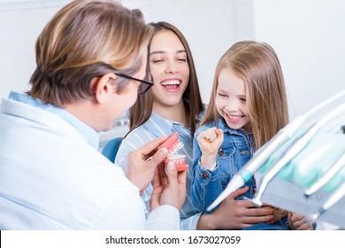 Little cute smiling girl is sitting in dental chair with mother in clinic, office. Doctor is preparing for examination of child teeth, talking with patient. Visiting dentist with children. - Powered by Shutterstock