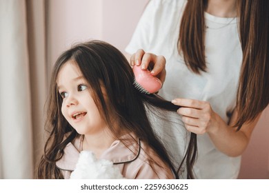 a little dark-haired girl looks into the camera and smiles while her mother combs her daughter's hair. hair care - Powered by Shutterstock