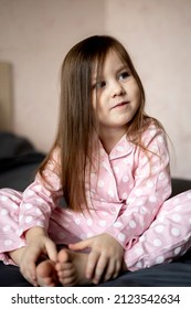 Little dark-haired girl in pink pajamas is sitting on the bed. Good morning. Happy family concept. Leisurely morning.