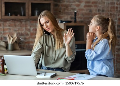 Little Daughter Asking Her Mom For Attention, Busy Mother Talking By Phone And Looking At Laptop, Kitchen Interior, Copy Space