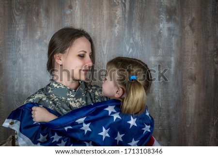 Little daughter covering soldier mother with US flag, happy with homecoming.