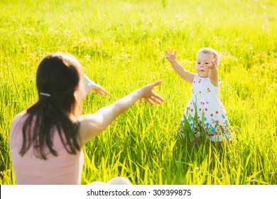  Little Daughter Happily Running Towards Her Mom. People Having Rest In Sunny Green Meadow On Spring Or Summer Day. Mother And Baby Playing Outside.