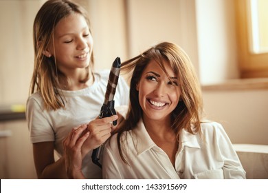 Little daughter is having fun playing hairdressing salon with her young mother, curling her hair with electric hair curler. - Powered by Shutterstock