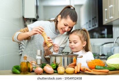 Little daughter helping cooking soup and mother add pepper to pan - Powered by Shutterstock