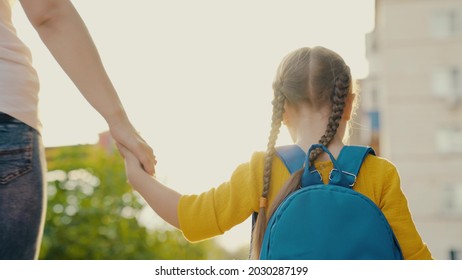 Little daughter, schoolgirl, walks down street with backpack, holds her mother's hand. Happy family, mother and child go to school together holding hands. Preschool education. Baby, girl goes to study