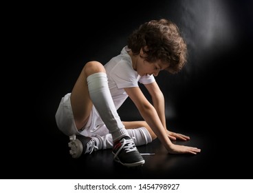 Little disappointed boy soccer player sitting on the floor with untied lace on the boot. Dark background - Powered by Shutterstock