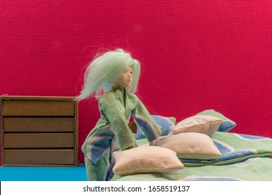 Little doll girl getting ready for bed in a pyjama matching with the bedding. Cardboard bed and dresser. Pink wall and blue floor. Room for copy.