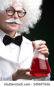 Little Einstein. Cheerful Little Boy Looking Like Einstein Holding A Bottle With Red Liquid While Isolated On Black