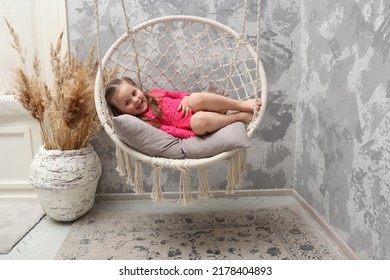 Little emotional girl rides on a swing in the children's room. Child 4-5 years old in the children's room. A baby in a pink dress lies on a round rope swing. The child plays alone in the room.