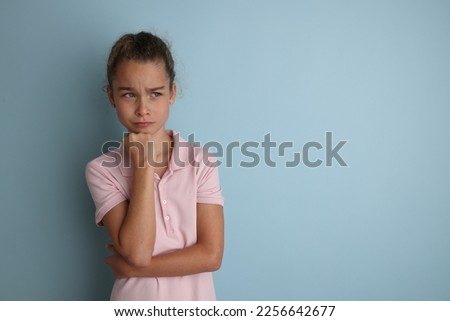 Little emotional teenage girl in pink shirt 11, 12 years old on an isolated blue background. Children's studio portrait. Place text to copy space for caption, advertising children's goods.