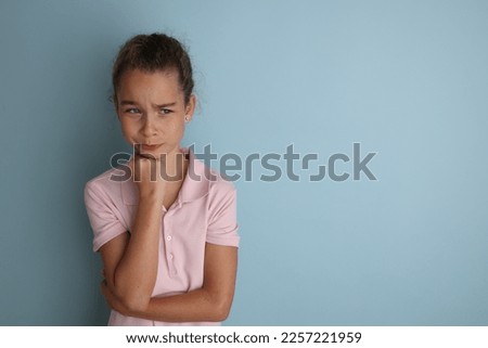 Little emotional teenage girl in pink shirt 11, 12 years old on an isolated blue background. Children's studio portrait. Place text to copy space for caption, advertising children's goods.