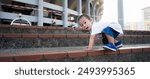 Little Explorer: A curious toddler in white shirt and blue jeans climbs a set of concrete steps, his eyes wide with wonder and determination. The backdrop of stadium adds sense of scale and adventure.