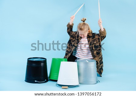 Little expressive blond boy drum music with iron and plastic buckets. Using all his force to make louder sound.