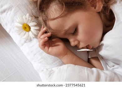 Una pequeña niña de cabello limpio con un pacificador duerme en una cuna. En las cercanías hay una flor de camomila como símbolo de buen sueño.