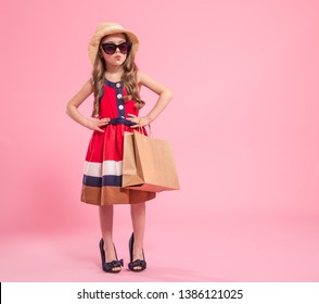 Little Fashionista With A Shopping Bag In A Summer Hat And Glasses , On A Colored Pink Background In Mom's Shoes , The Concept Of Children's Fashion