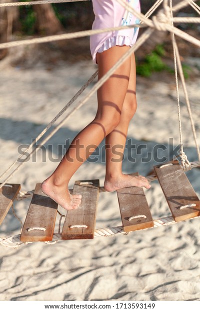 Little feet of a child walk on a rope bridge on\
the beach in the sunset.