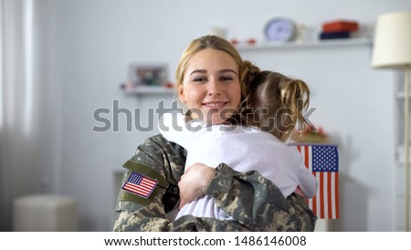 Little female kid with US flag embracing soldier mother, family reunion, patriot