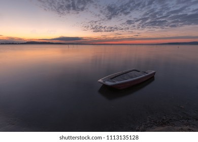 A Little Fishing Boat In The Middle Of Perfectly Still Water At 